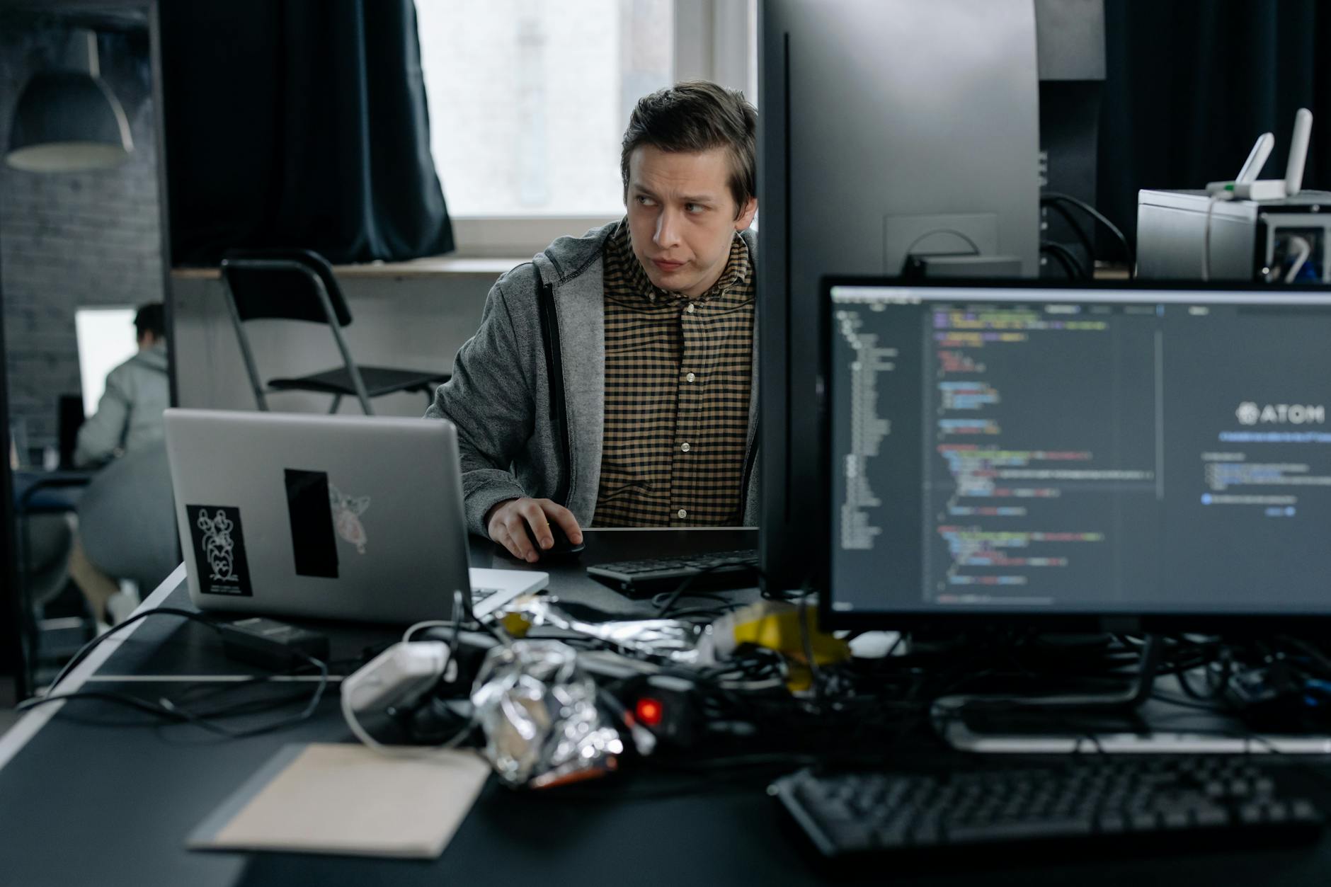 A developer sitting in front of a laptop, staring blankly at the code editor on a quiet office screen