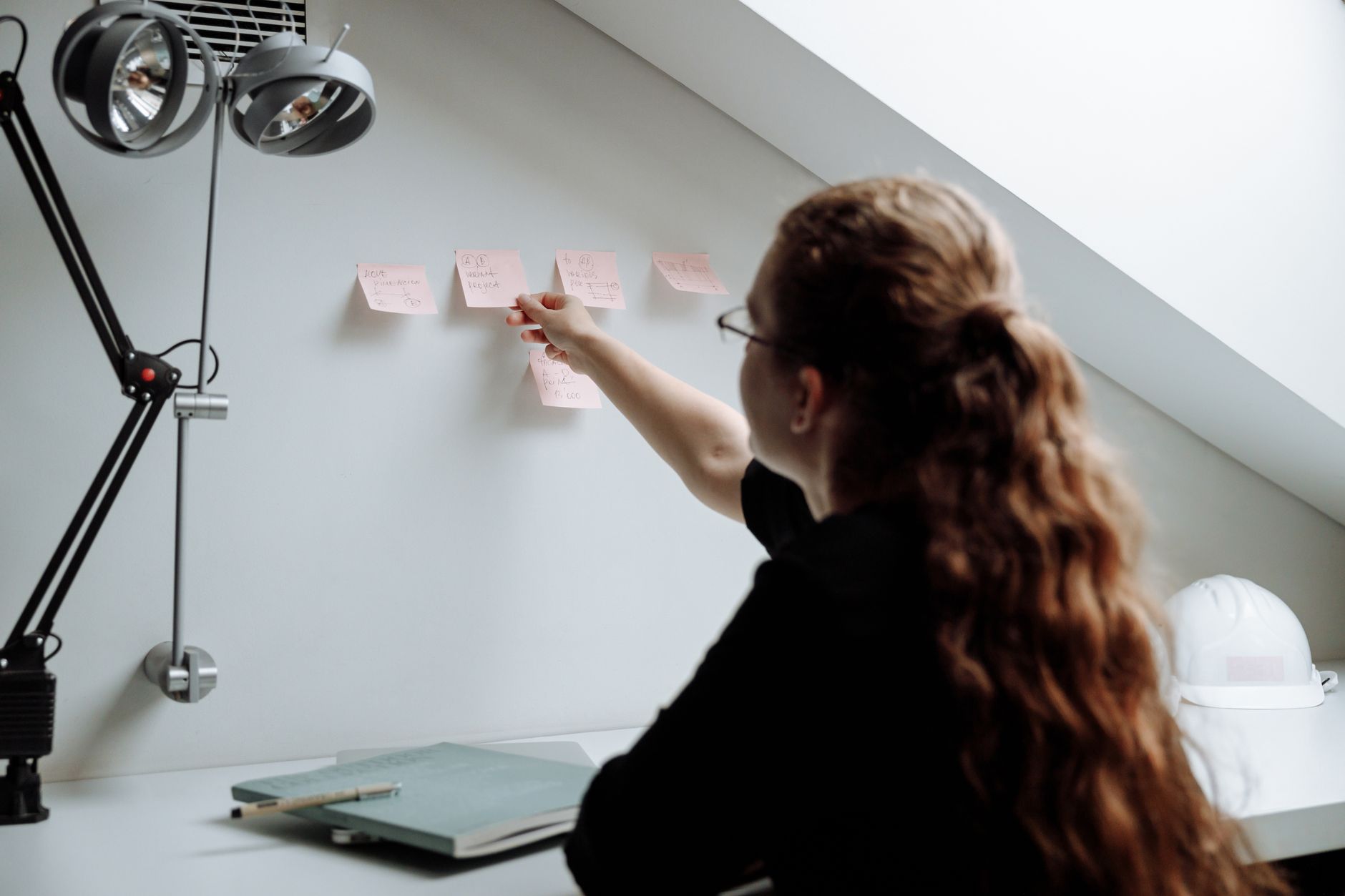 A person writing a one-page vendor risk summary at a desk, with sticky notes of AI tool names pinned to the wall behind