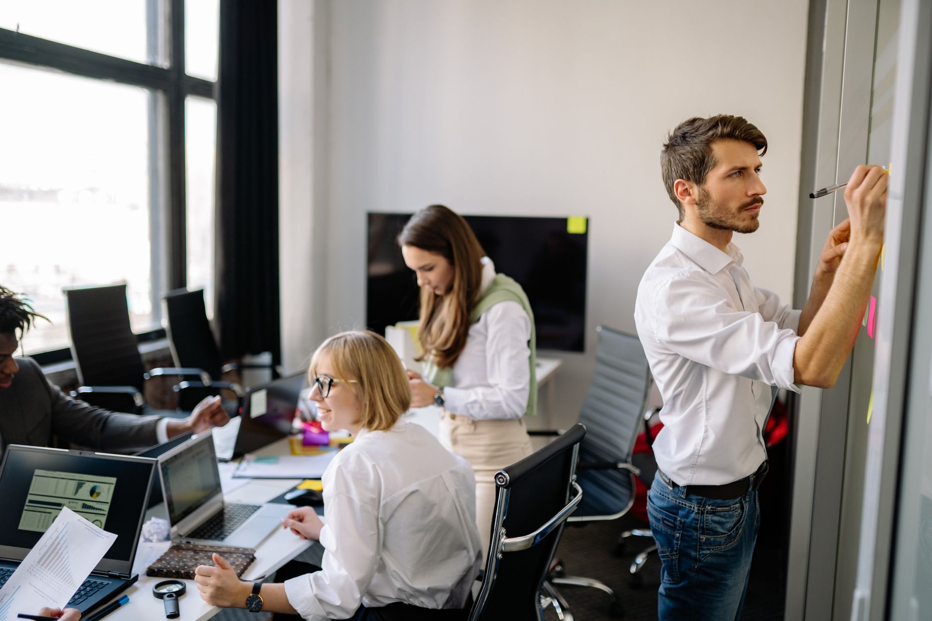 A software development team collaborating around a white board filled with flowcharts and user-experience wireframes, with warm sunlight streaming through the windows.