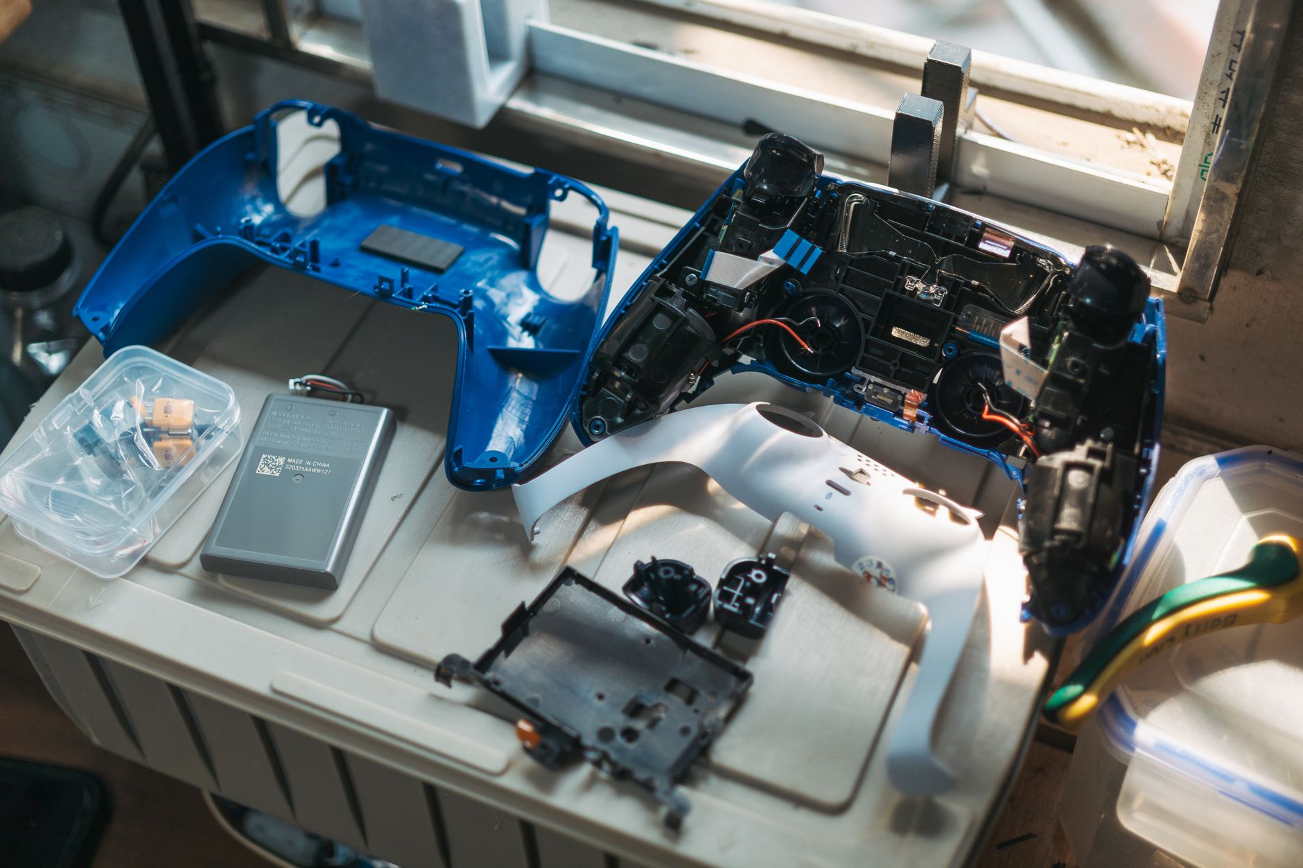 A modern handheld gaming console on an engineering desk, partially disassembled to show a modular, easily removable battery pack with a simple latch system, realistic studio lighting
