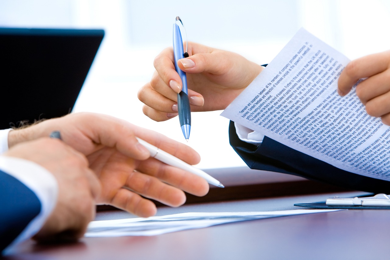 An export manager editing an AI-generated draft email on a laptop, handwriting notes beside it, focused and deliberate