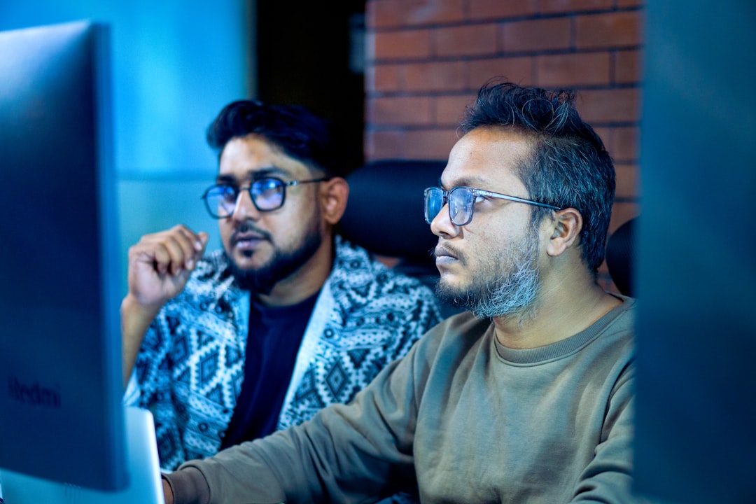 Two or three people gathered around a monitor in a small startup office, talking quietly